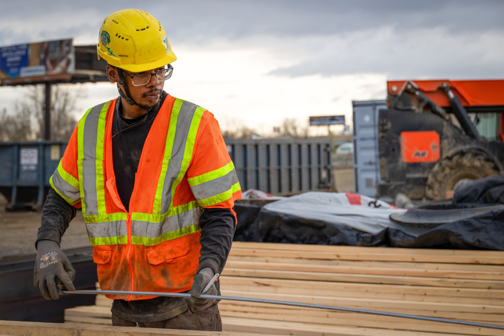 3T5A2363-2 Union carpenter in safety gear measuring wood on job site.