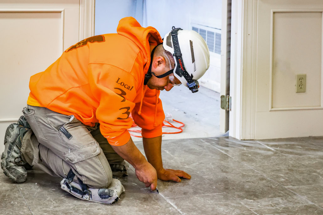 Flooring_CLE Union floor layer on knees cutting seams on newly install tiles.